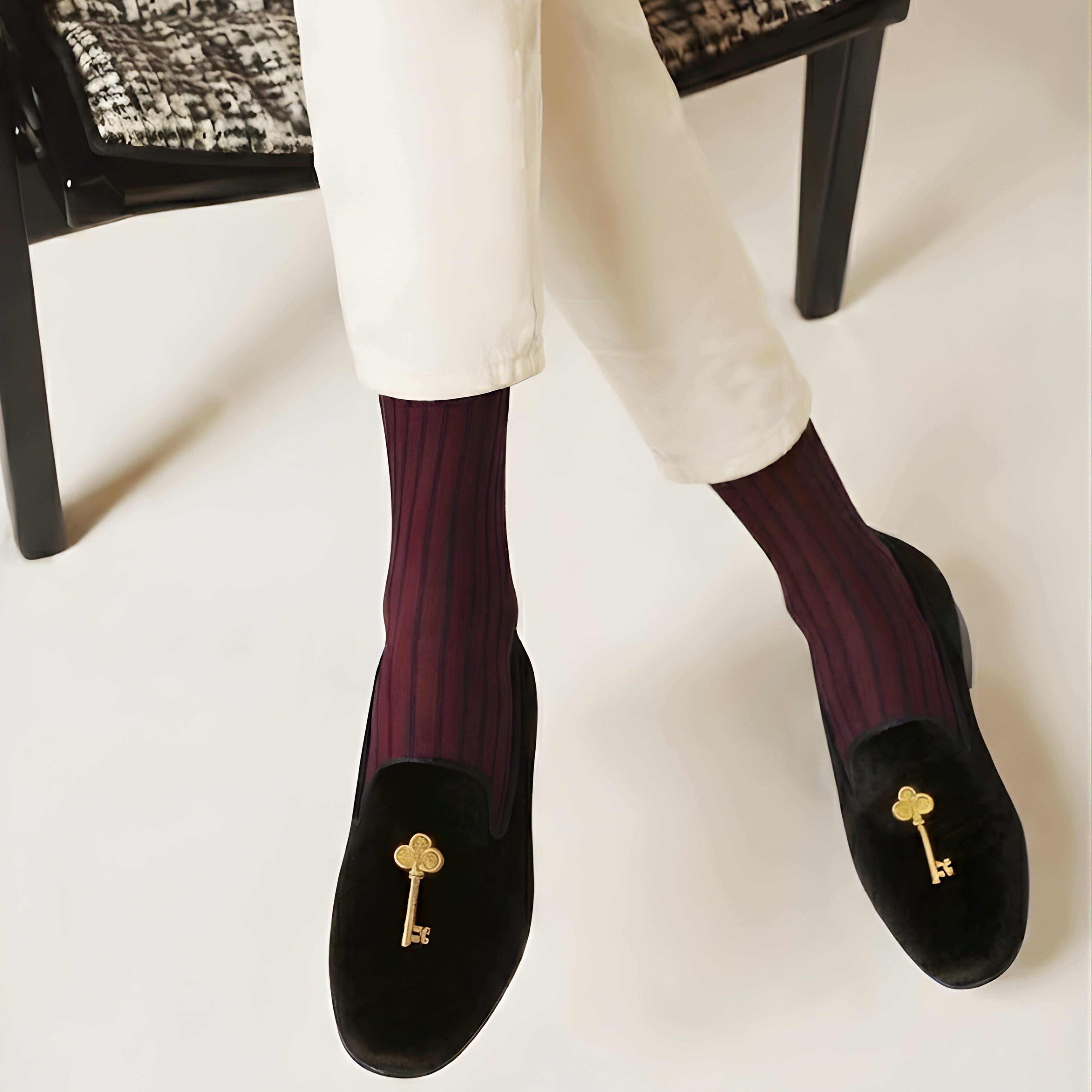 Person wearing black loafers with gold key embellishments and purple socks on a white background