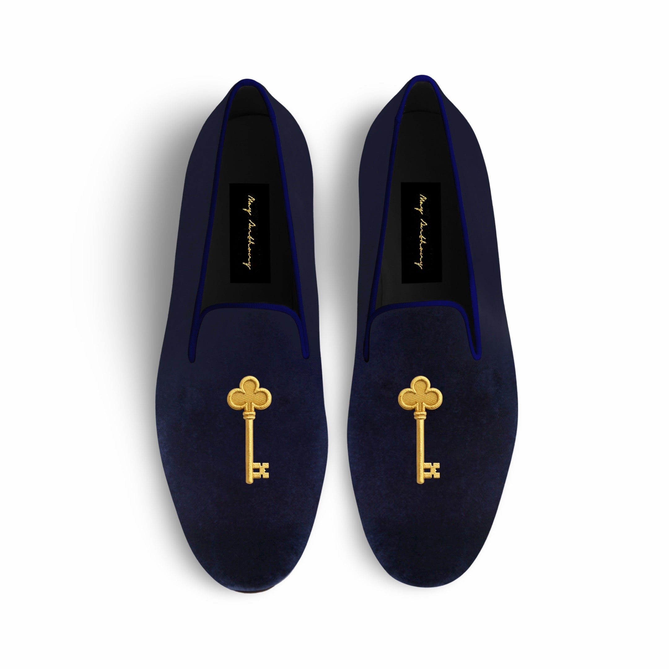 Pair of navy velvet slippers with gold key embellishments on a white background