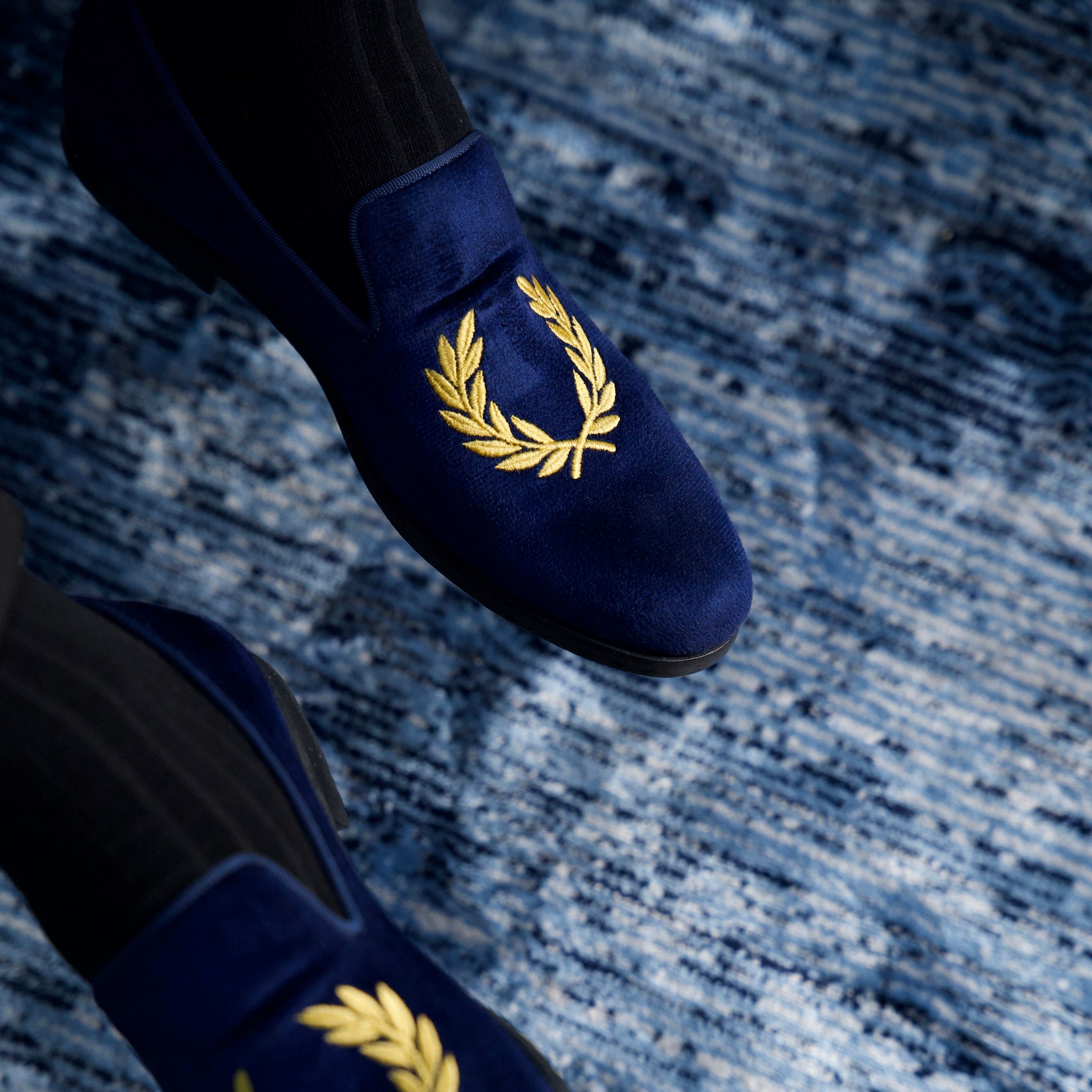 Navy blue loafers with gold laurel wreath design on a textured blue surface