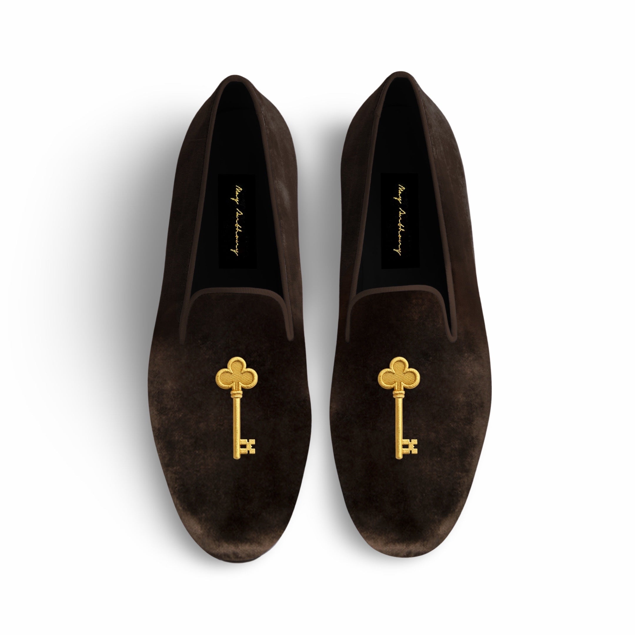 Brown suede loafers with gold key embellishments on a white background