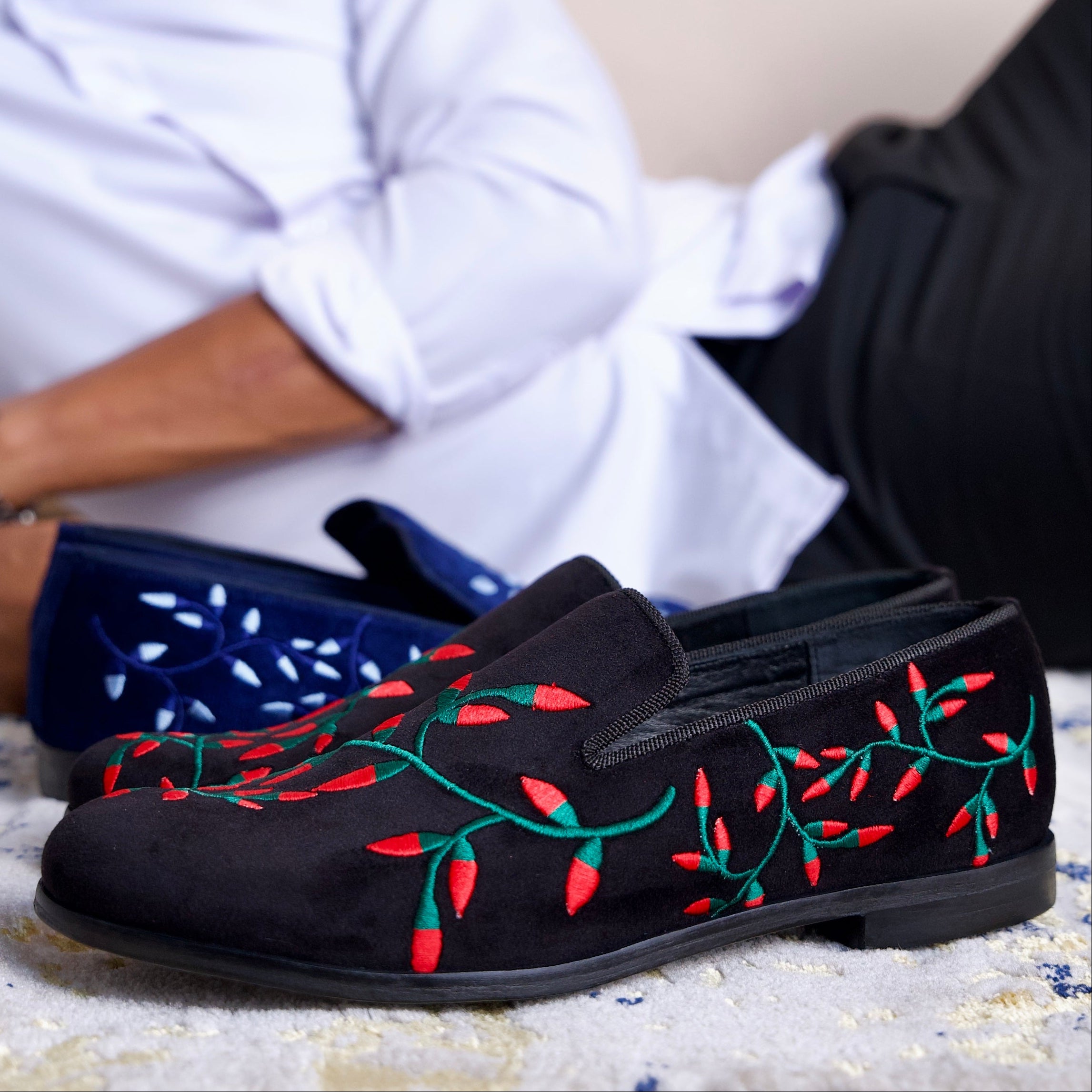 Black loafers with red and green embroidery on a textured surface.